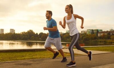 Homem e mulher sorrindo enquanto correm em trilha pavimentada à beira do lago ao entardecer.