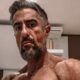 Marcos Mion sem camisa, com barba e cabelo grisalho, olhando diretamente para a câmera.