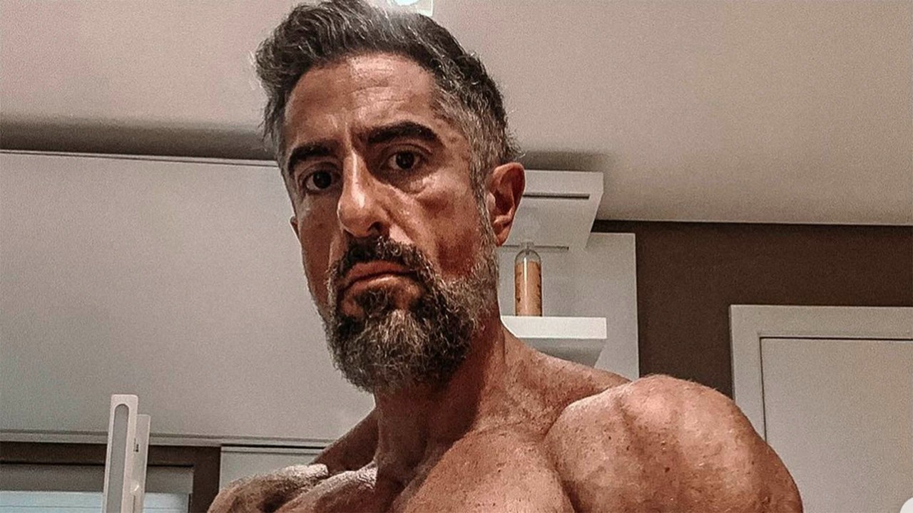 Marcos Mion sem camisa, com barba e cabelo grisalho, olhando diretamente para a câmera.