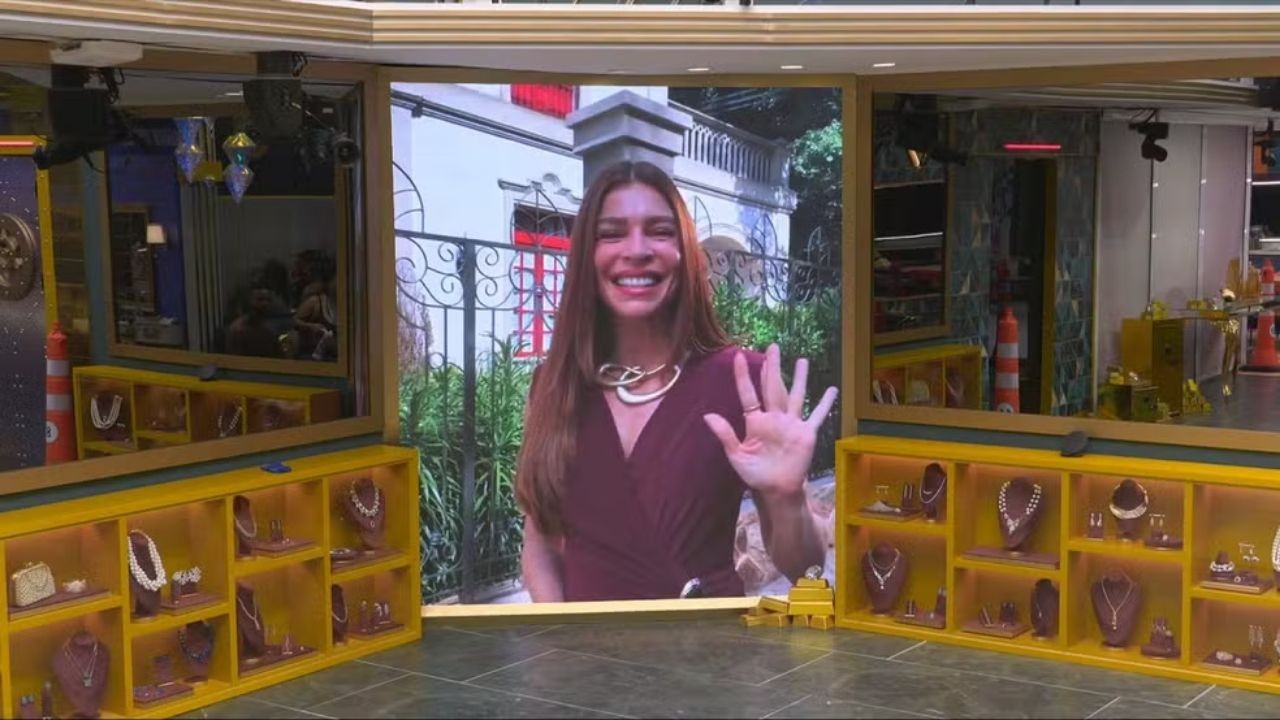 Grazi Massafera sorrindo e acenando em tela gigante, em cenário com joias e espelhos.