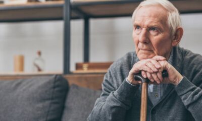 Homem idoso de cabelos brancos, sentado, olhando pensativo, com as mãos sobre uma bengala.
