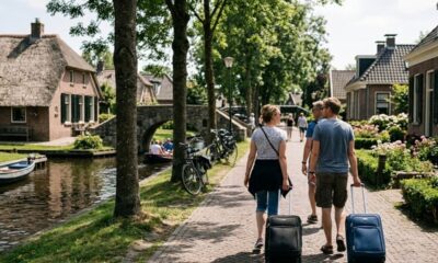 Pessoas com malas caminhando em uma vila holandesa com canais, barcos e casas.