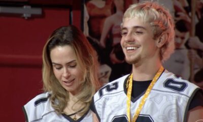 Duas pessoas sorrindo em camisas brancas e pretas; o homem usa um cordão amarelo.