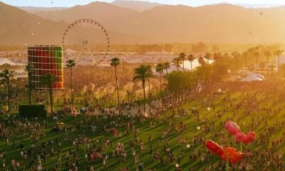 Vista aérea do festival Coachella com multidão, roda-gigante, arte e palmeiras ao pôr do sol.