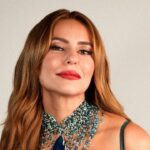 Paolla Oliveira com cabelos castanhos, batom vermelho e colar de contas azuis, olhando para frente.