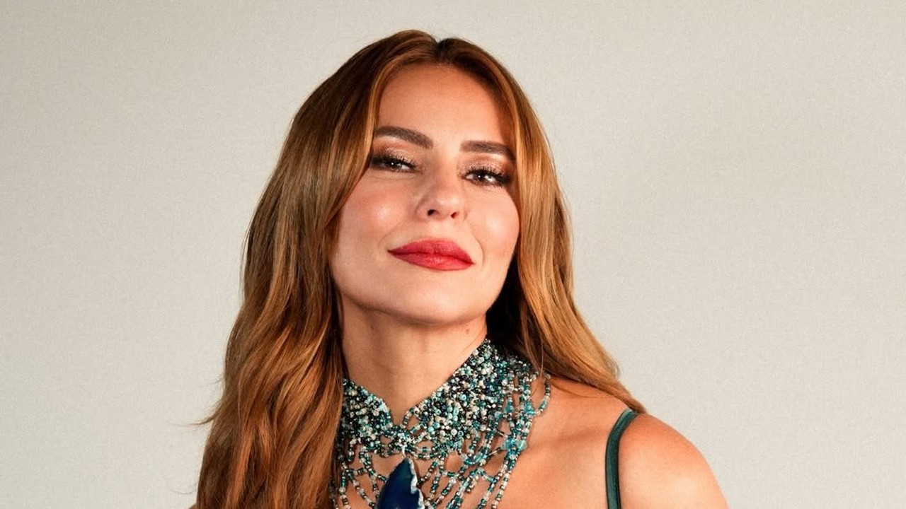 Paolla Oliveira com cabelos castanhos, batom vermelho e colar de contas azuis, olhando para frente.