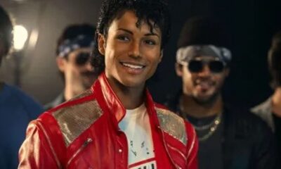 Jaafar Jackson sorrindo, vestido como Michael Jackson, usando jaqueta vermelha e cabelo cacheado.