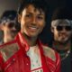 Jaafar Jackson sorrindo, vestido como Michael Jackson, usando jaqueta vermelha e cabelo cacheado.