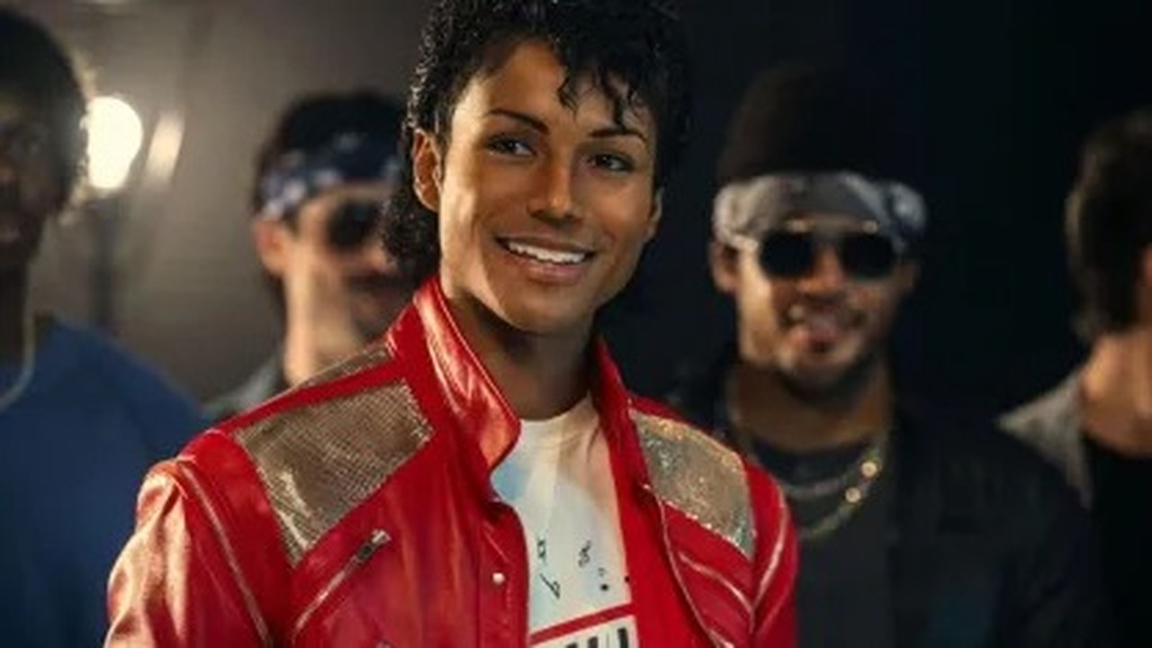 Jaafar Jackson sorrindo, vestido como Michael Jackson, usando jaqueta vermelha e cabelo cacheado.