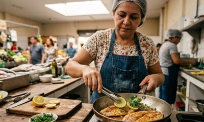 Mulher em avental cozinha filés de peixe em frigideira com limão e ervas.