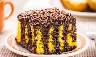 Fatia de bolo de cenoura com calda de chocolate e granulado em um prato branco.