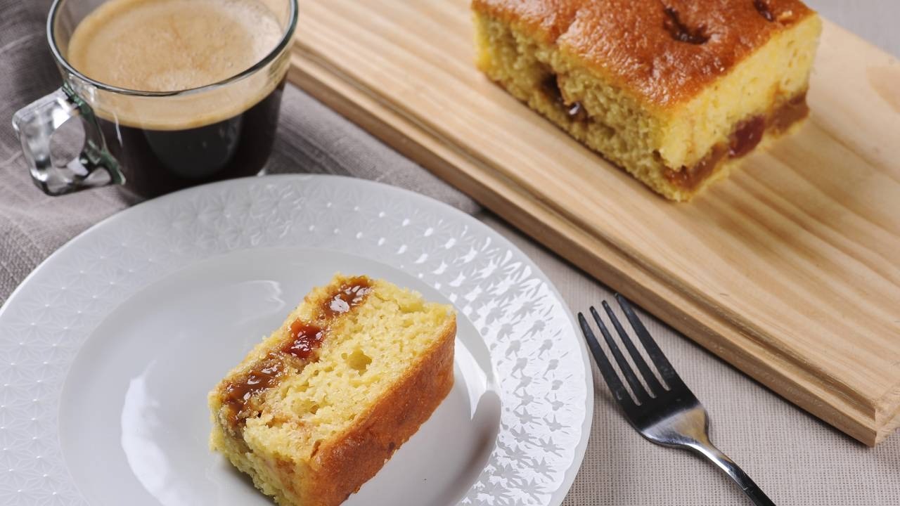 Fatia de bolo com recheio em prato branco, garfo, e xícara de café.