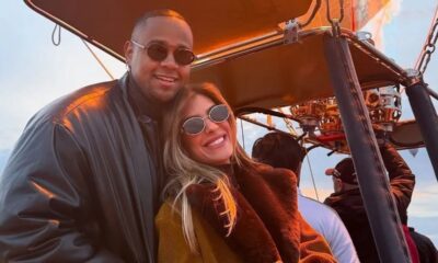 Lorena Improta e Léo Santana sorrindo em óculos escuros, juntos em um balão de ar quente.