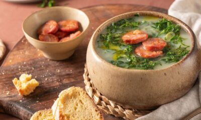 Caldo verde em tigela rústica com couve, linguiça calabresa, azeite e fatias de pão.