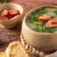 Caldo verde em tigela rústica com couve, linguiça calabresa, azeite e fatias de pão.