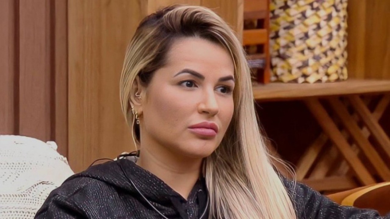 Mulher loira, Deolane Bezerra, agasalho preto, olhando à direita, expressão neutra.