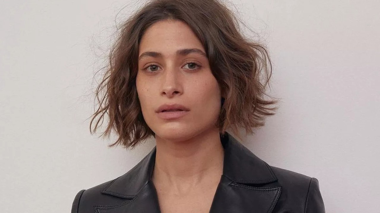 Close-up de mulher com cabelo castanho curto, blazer preto e expressão séria, olhando para frente.