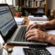 Pessoa digita em laptop com gov.br, "Programa Gerador da Declaração", calculadora e café na mesa.