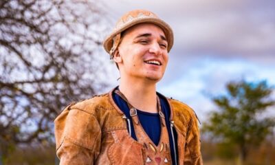 João Gomes sorri, usando chapéu e colete de couro, em ambiente externo.