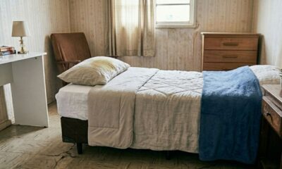 Travesseiro branco com grande mancha amarela sobre uma cama simples em um quarto antigo.