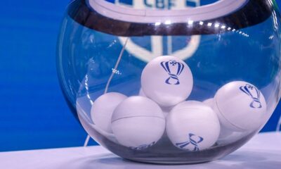 Globo de vidro transparente com bolas brancas exibindo logotipo de troféu azul, em fundo azul.