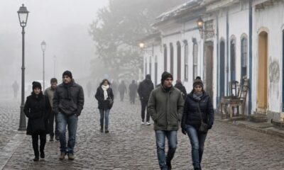Várias pessoas agasalhadas caminham em rua de paralelepípedos sob forte neblina em cidade histórica.