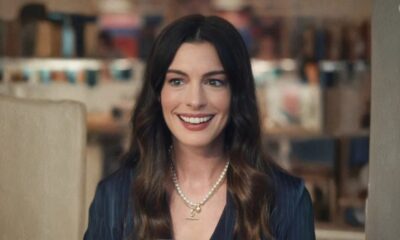 Close-up de Anne Hathaway sorrindo, com cabelo castanho escuro e colar de pérolas.