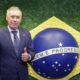 Carlo Ancelotti sorri, polegar para cima, ao lado do globo da bandeira brasileira.