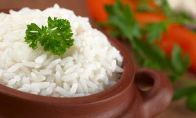 Close-up de arroz branco cozido em tigela de barro, com um ramo de salsinha.