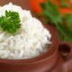Close-up de arroz branco cozido em tigela de barro, com um ramo de salsinha.