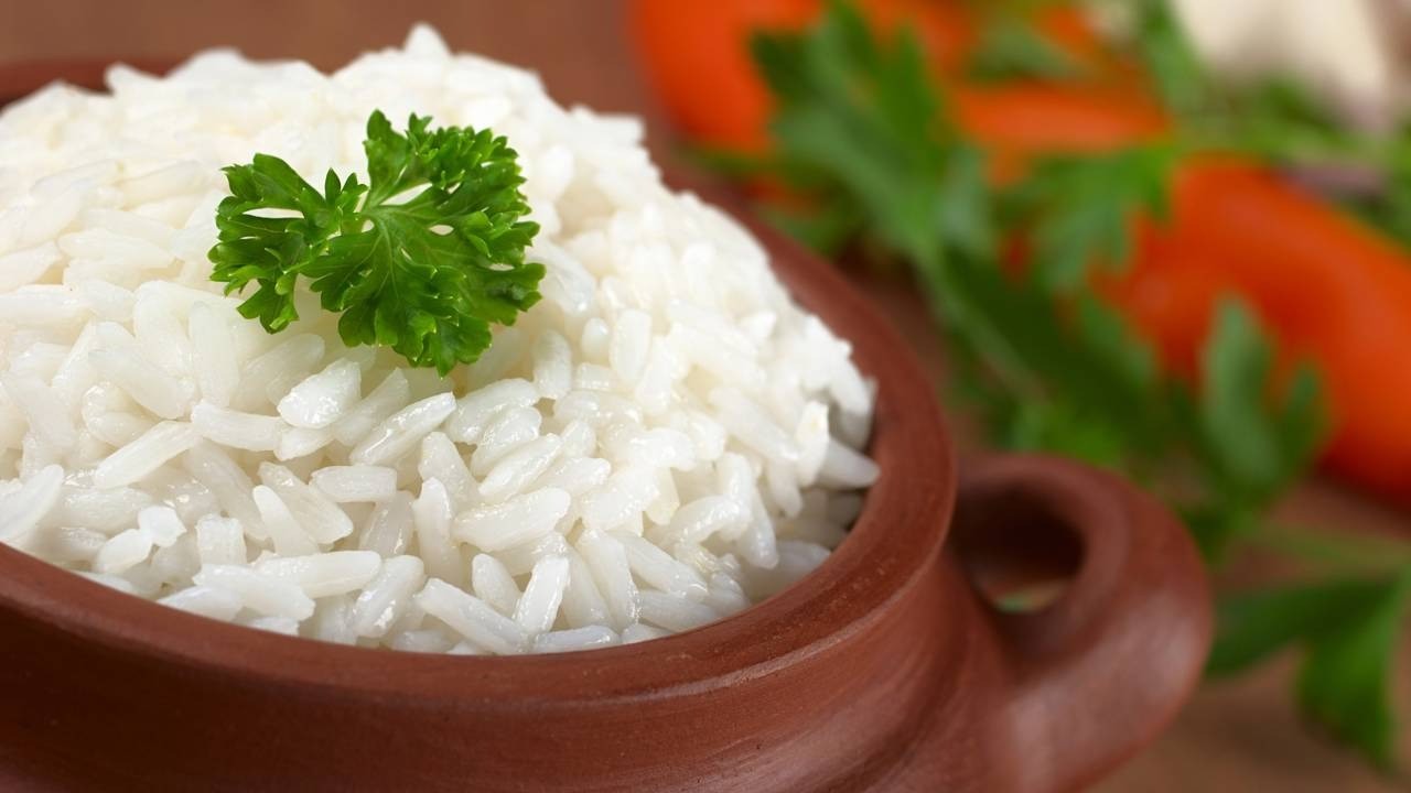 Close-up de arroz branco cozido em tigela de barro, com um ramo de salsinha.