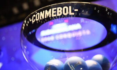 Recipiente de vidro com 'CONMEBOL' escrito e bolas azuis de sorteio 'Sudamericana'.