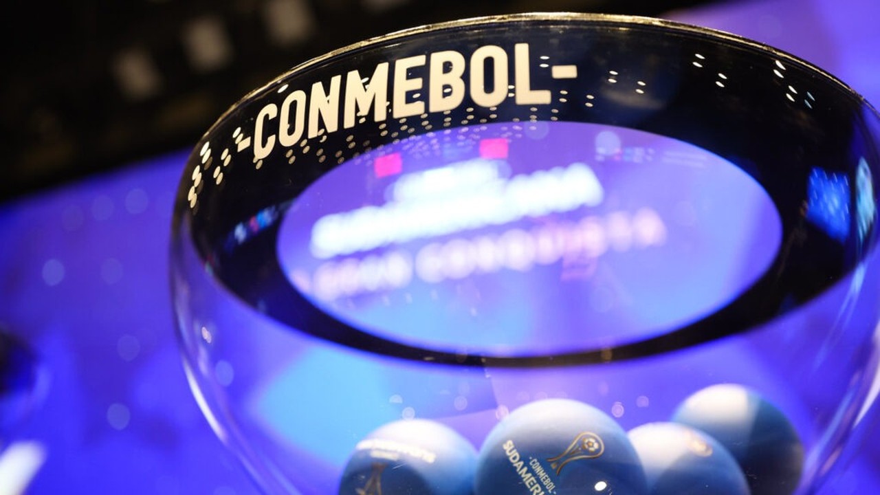 Recipiente de vidro com 'CONMEBOL' escrito e bolas azuis de sorteio 'Sudamericana'.