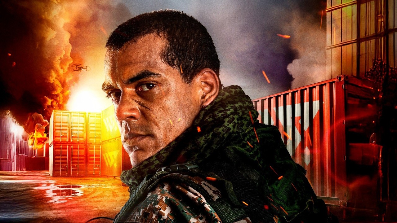 Close-up de homem com cicatrizes e uniforme tático, em ambiente com fogo e contêineres.