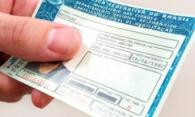 Mão segura CNH brasileira com nome Nicolas, data de nascimento e validade em destaque.