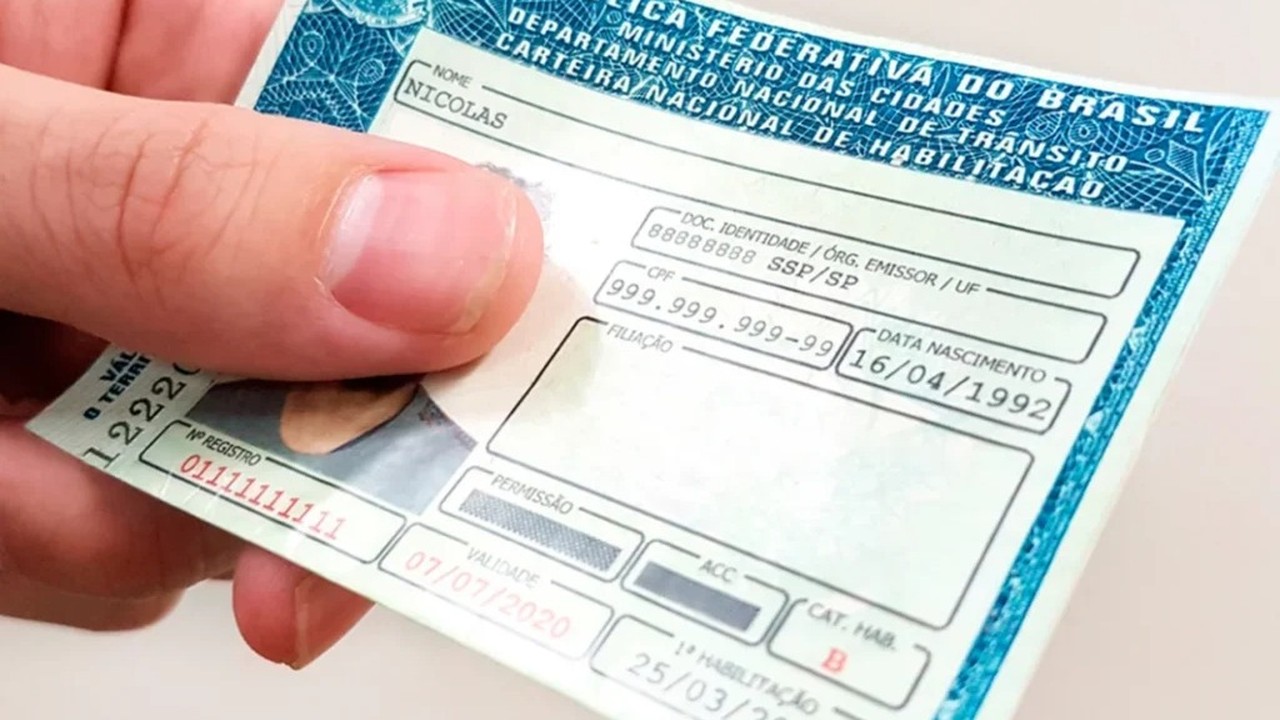 Mão segura CNH brasileira com nome Nicolas, data de nascimento e validade em destaque.