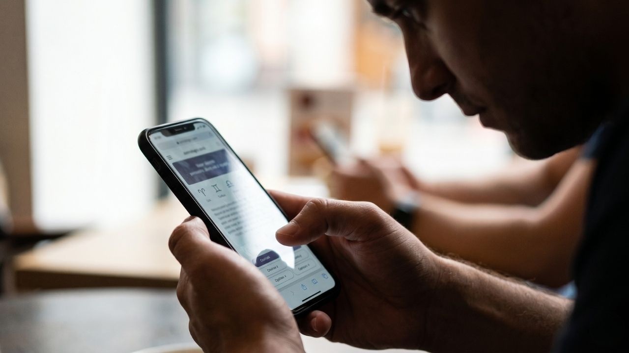 Homem segura smartphone com as duas mãos, navegando em tela que exibe símbolos astrológicos.