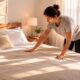 Pessoa arrumando a cama em quarto iluminado pela manhã, ambiente simples e organizado