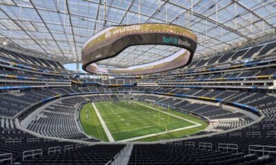 Interior do SoFi Stadium, Los Angeles, com campo, arquibancadas e telão 'SoFi Stadium', 'Hyundai', 'Samsung'.