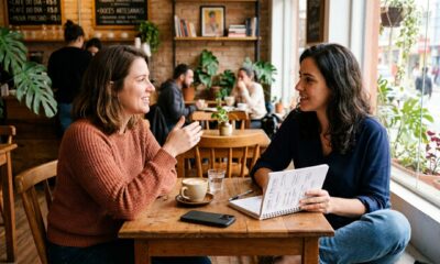 Duas pessoas conversando em ambiente neutro, uma delas ouvindo atentamente com postura aberta enquanto segura um caderno de ideias, celular virado para baixo na mesa, cena realista mostrando mente aberta sem necessidade de aprovação externa. Em caso de textos na imagem, ele deve estar em PT-BR