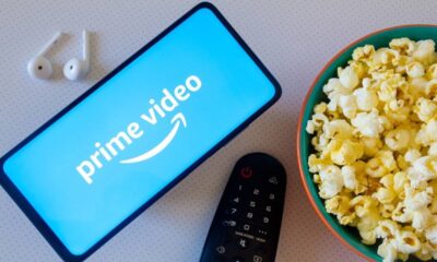 Celular com logo Prime Video, fones de ouvido, controle remoto e tigela de pipoca.