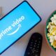 Celular com logo Prime Video, fones de ouvido, controle remoto e tigela de pipoca.