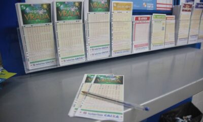 Displays de loteria da Caixa com volantes como Mega da Virada e uma caneta sobre o balcão.