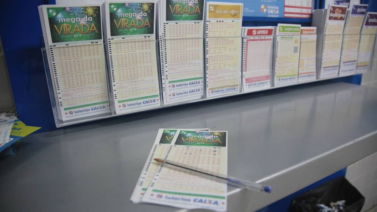 Displays de loteria da Caixa com volantes como Mega da Virada e uma caneta sobre o balcão.