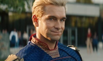 Close-up de Homelander, um homem loiro de olhos azuis em uniforme de super-herói, sorrindo.