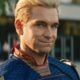 Close-up de Homelander, um homem loiro de olhos azuis em uniforme de super-herói, sorrindo.