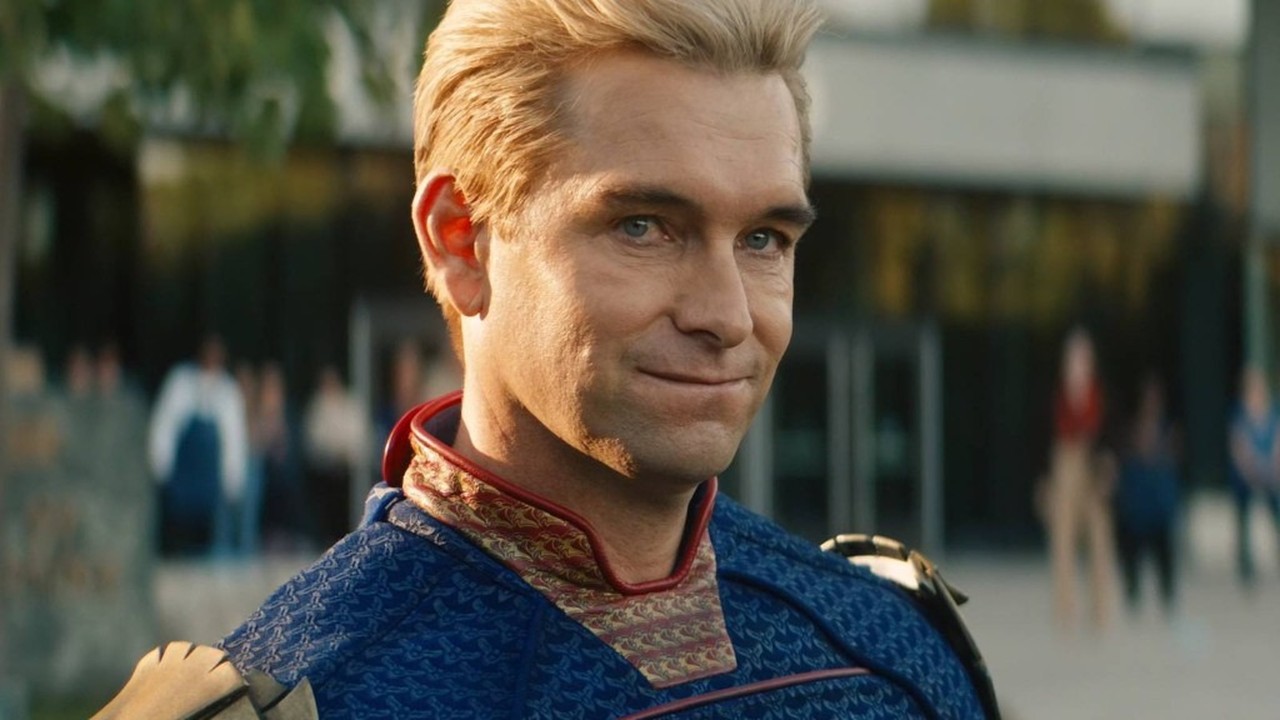 Close-up de Homelander, um homem loiro de olhos azuis em uniforme de super-herói, sorrindo.