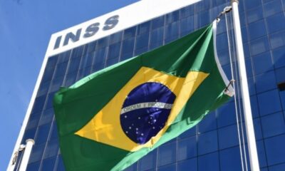 Prédio do INSS com a bandeira do Brasil e "ORDEM E PROGRESSO" tremulando.