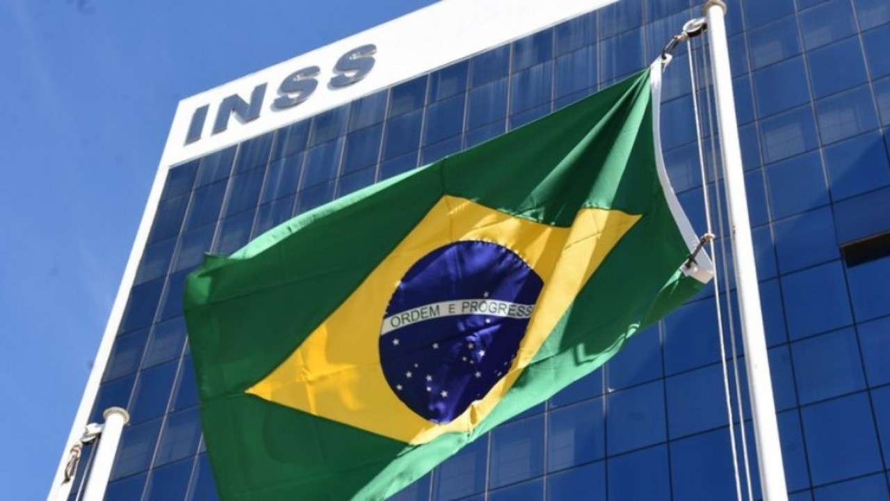 Prédio do INSS com a bandeira do Brasil e "ORDEM E PROGRESSO" tremulando.