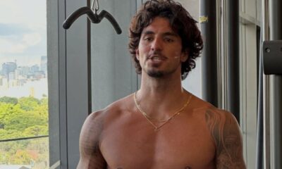 Gabriel Medina, sem camisa, cabelo e barba, falando, em academia com fundo urbano.